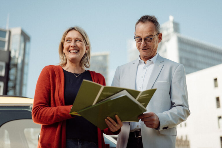 Eine Frau und ein Mann aus dem Vertriebs besprechen etwas und stehen dabei vor einem Bürogebäude.