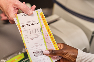 Die Hand einer Person übergibt eine LOTTO-Spielquittung in die Hand einer anderen Person.