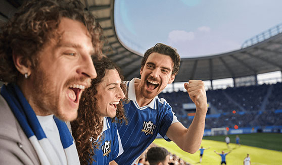 Drei Freunde stehen auf der VIP-Tribüne im Fußballstadion und jubeln.