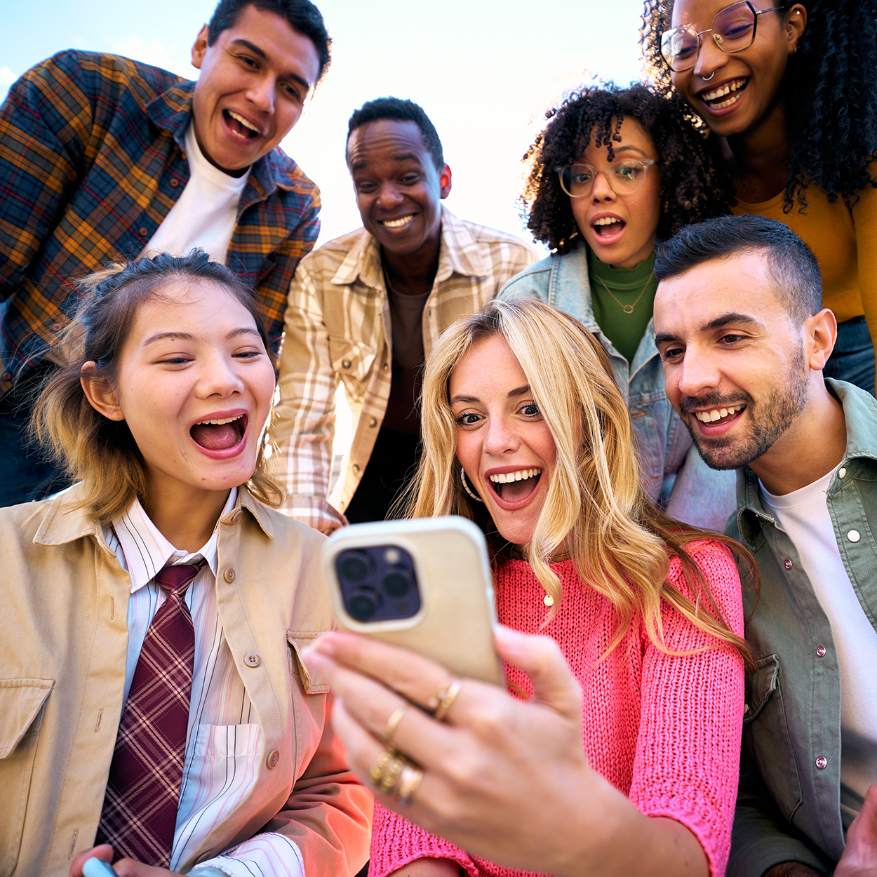 Eine Gruppe von Freunden sitzen zusammen und schauen gespannt und freudig auf ein Smartphone.