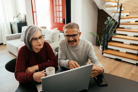 Aelteres Paar sitzt gemeinsam vor einem Laptop.