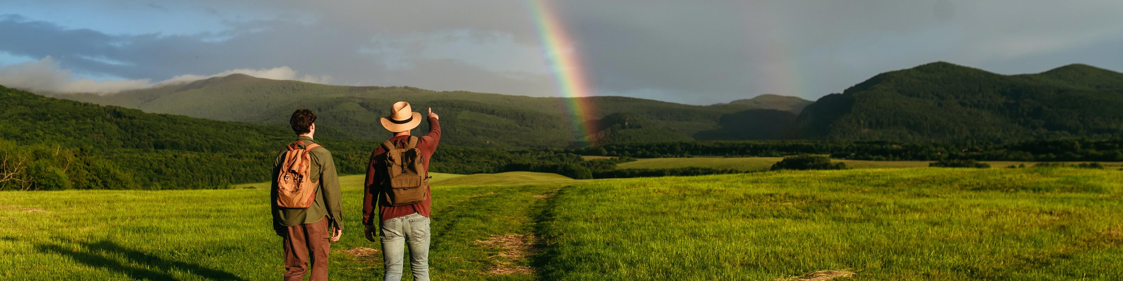 Zwei Menschen gehen wandern und sehen am Horizont einen Regenbogen.