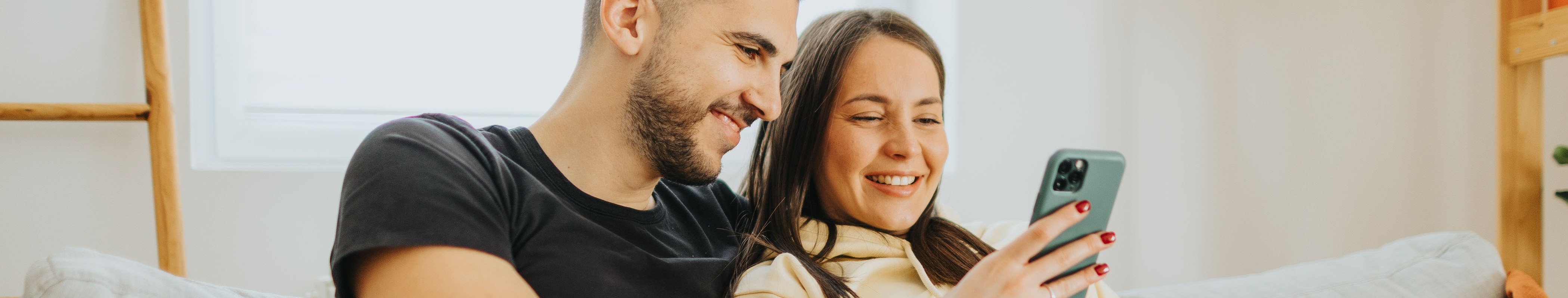 Ein Pärchen sitzt gemeinsam auf der Couch und schauen gemeinsam auf ein Smartphone.