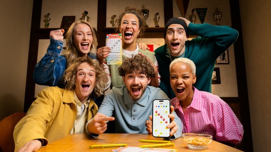 Gruppe von sechs Personen hat Spaß beim Bingo-Spiel mit Smartphone und Bingo-Los.