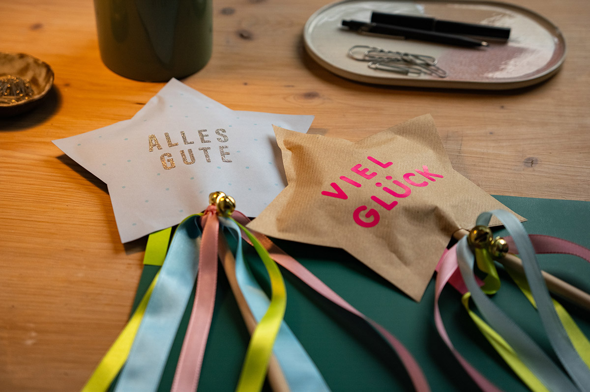 Zwei gebastelte Sterne mit Satinbändern und kleinen Glöckchen an einem Holzstock - WestLotto DIY-Idee