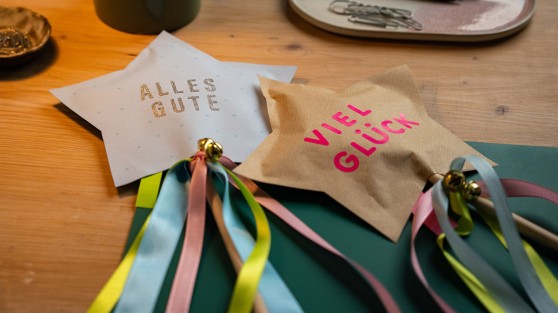 Zwei gebastelte Sterne mit Satinbändern und kleinen Glöckchen an einem Holzstock - WestLotto DIY-Idee