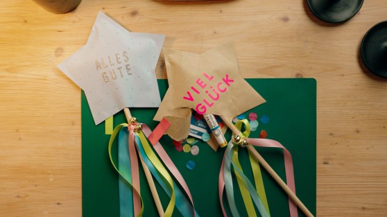 Zwei gebastelte Sterne mit Satinbändern und kleinen Glöckchen an einem Holzstock - WestLotto DIY-Idee GlücksSpirale