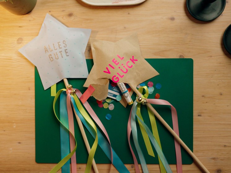 Zwei gebastelte Sterne mit Satinbändern und kleinen Glöckchen an einem Holzstock - WestLotto DIY-Idee GlücksSpirale