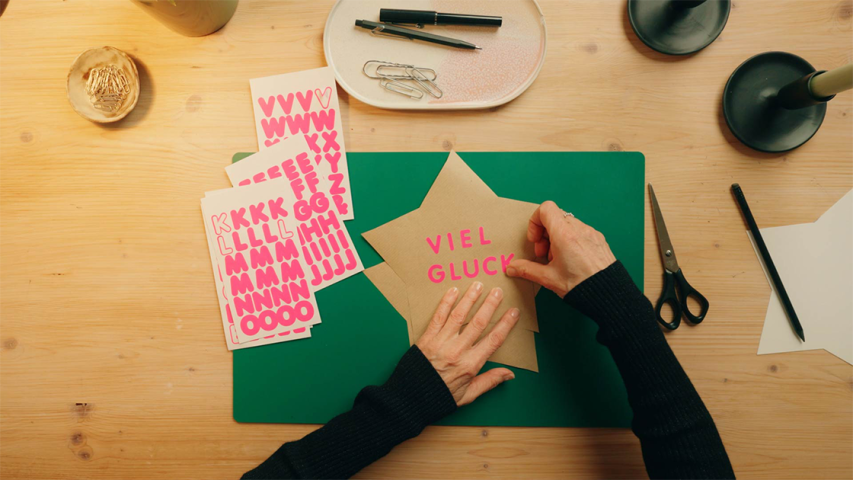 Pinke Klebe-Buchstaben werden auf einen Stern aus Kraftpapier geklebt - WestLotto DIY-Idee
