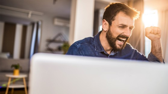 Mann sitzt vor Monitor und jubelt | Euojackpot-Gewinner NRW