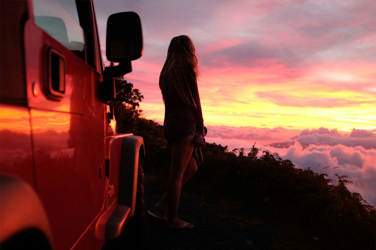 Frau steht auf Berg und schaut sich Sonnenuntergang an. WestLotto