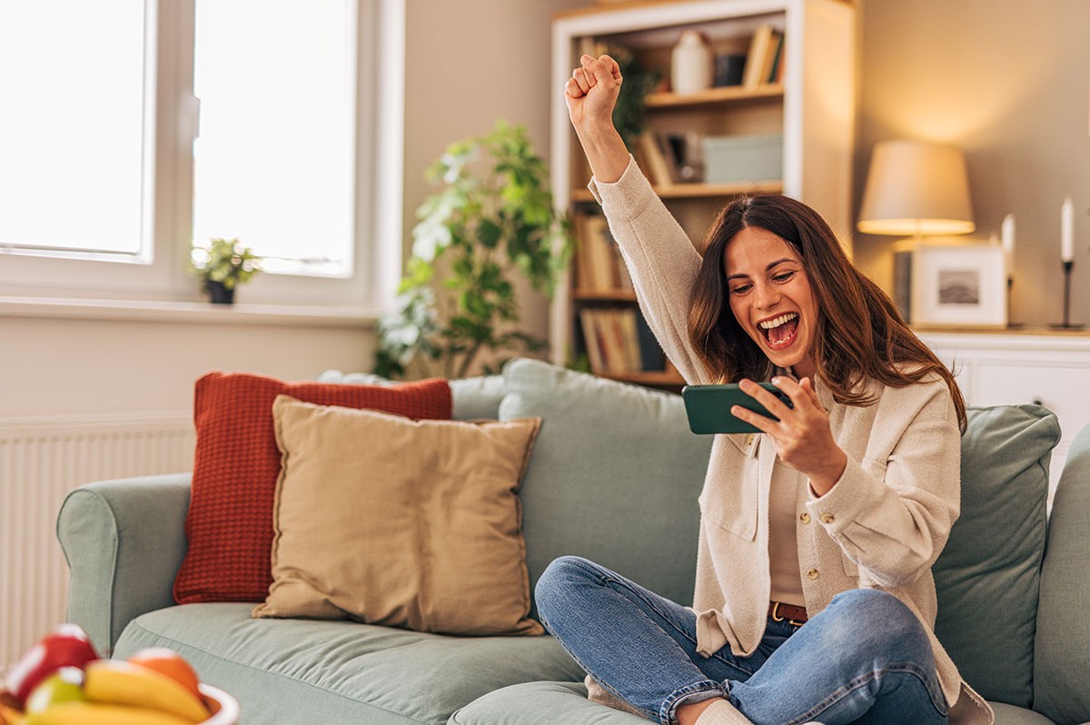 Frau sitzt auf dem Sofa und jubelt - WestLotto Gewinnerbilanz 