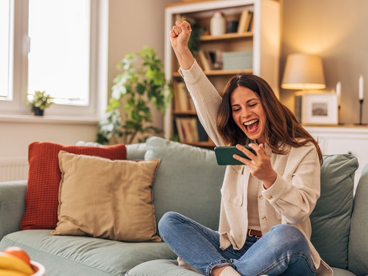 Frau sitzt auf dem Sofa und jubelt - WestLotto Gewinnerbilanz 