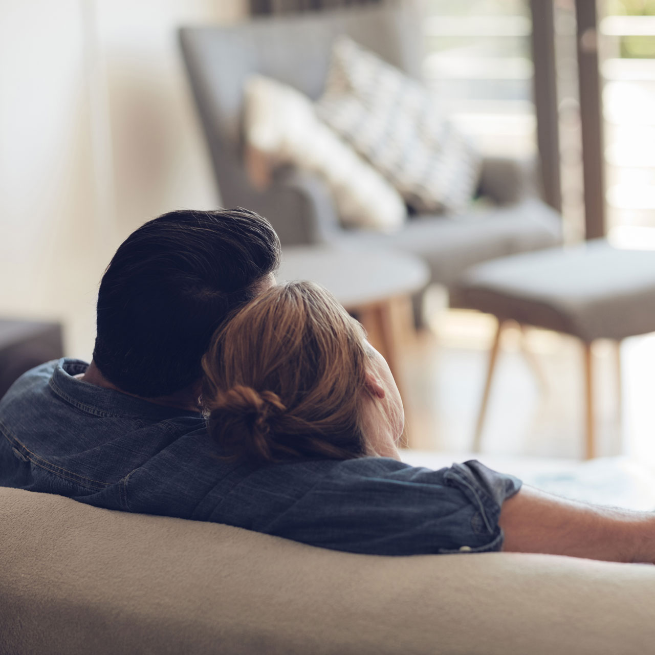 Von hinten fotografiertes Pärchen sitzt auf Couch und schaut aus dem Fenster | Gewinner WestLotto-Rubbellos Mückenjagd
