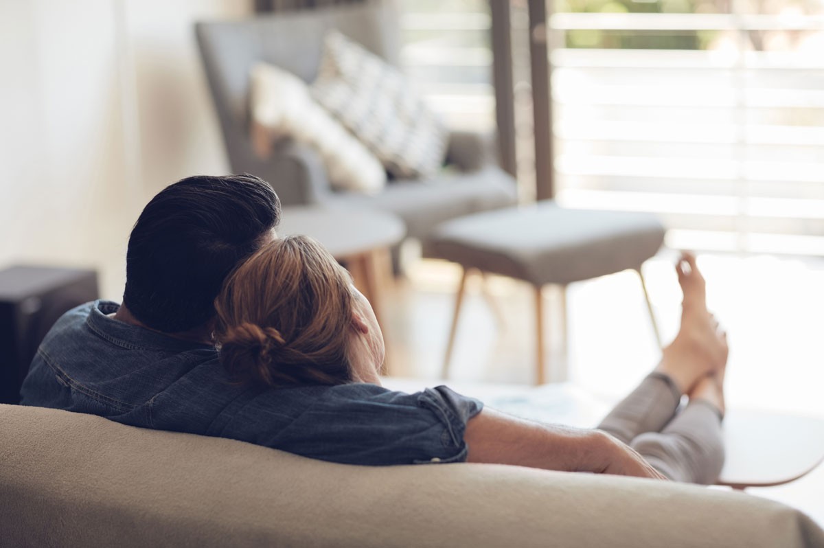 Von hinten fotografiertes Pärchen sitzt auf Couch und schaut aus dem Fenster | Gewinner WestLotto-Rubbellos Mückenjagd