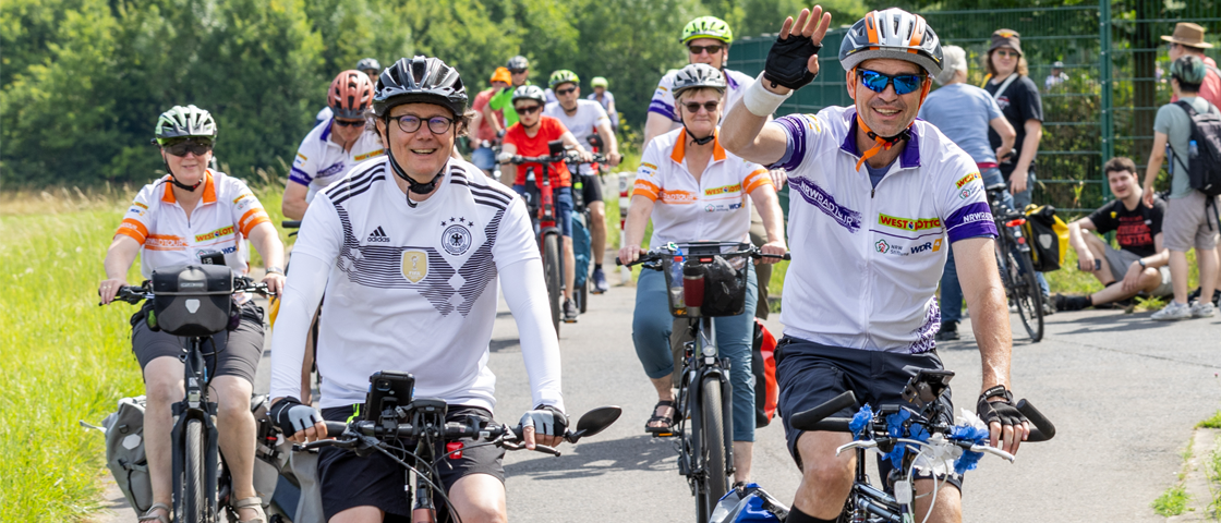 Radfahrer grüßen in die Kamera | WestLotto NRW-Radtour