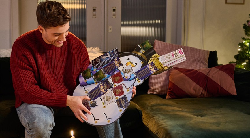 Mann sitzt auf einer Couch und hält einen Rubbellos-Adventskalender von WestLotto in den Händen