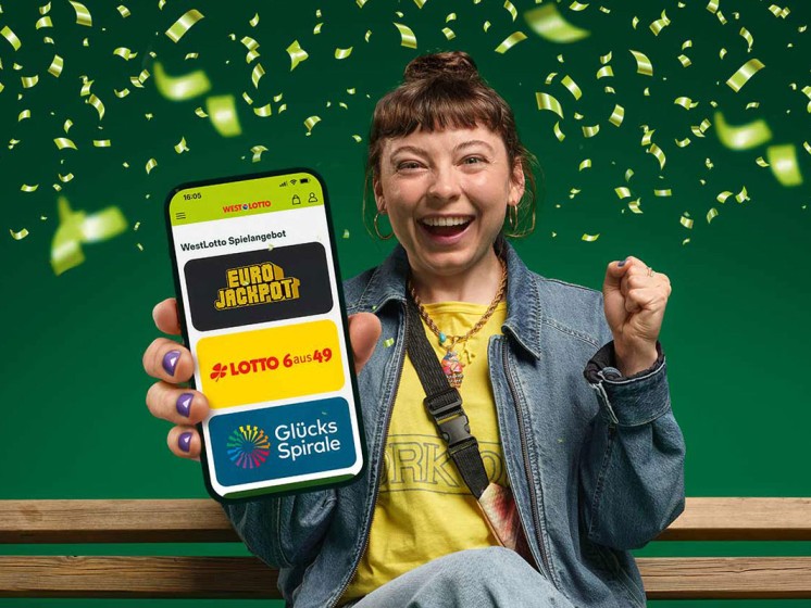 Jubelnde Frau hält Smartphone in der Hand, auf dem WestLotto-App geöffnet ist. Drumherum fliegt grünes Konfetti. 