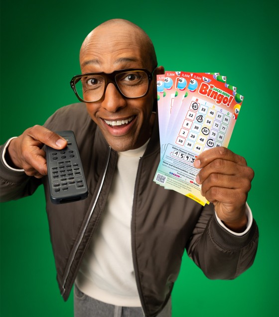 Amiaz Habtu - Moderator der Local Hero Bingo!-Show - hält Bingo!-Lose und Fernbedienung hoch. WestLotto