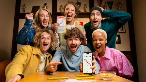 Gruppe von Menschen in einer Kneipe spielen Local Hero Bingo! mit App und Spielschein. WestLotto
