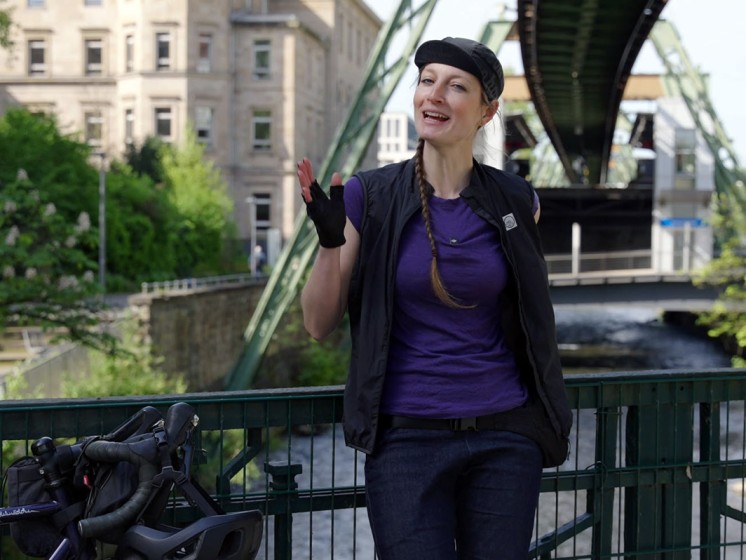 Radfahrerin steht vor Schwebebahn in Wuppertal | WestLotto Radtour des Monats