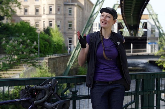 Radfahrerin steht vor Schwebebahn in Wuppertal | WestLotto Radtour des Monats