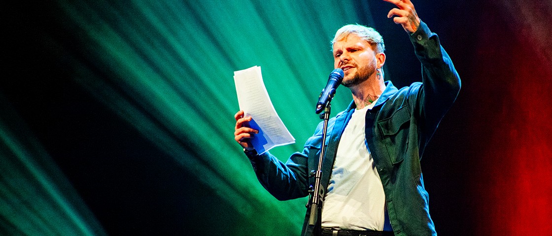 Poetry-Slammer hält Zettel in der Hand und spricht in Mikrofon - WestLotto