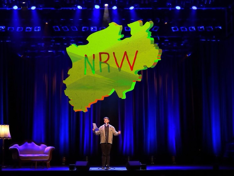 Wort-Künstler Flo Stein auf der Bühne mit Grafik der NRW-Landkarte | WestLotto Poetry-Slam