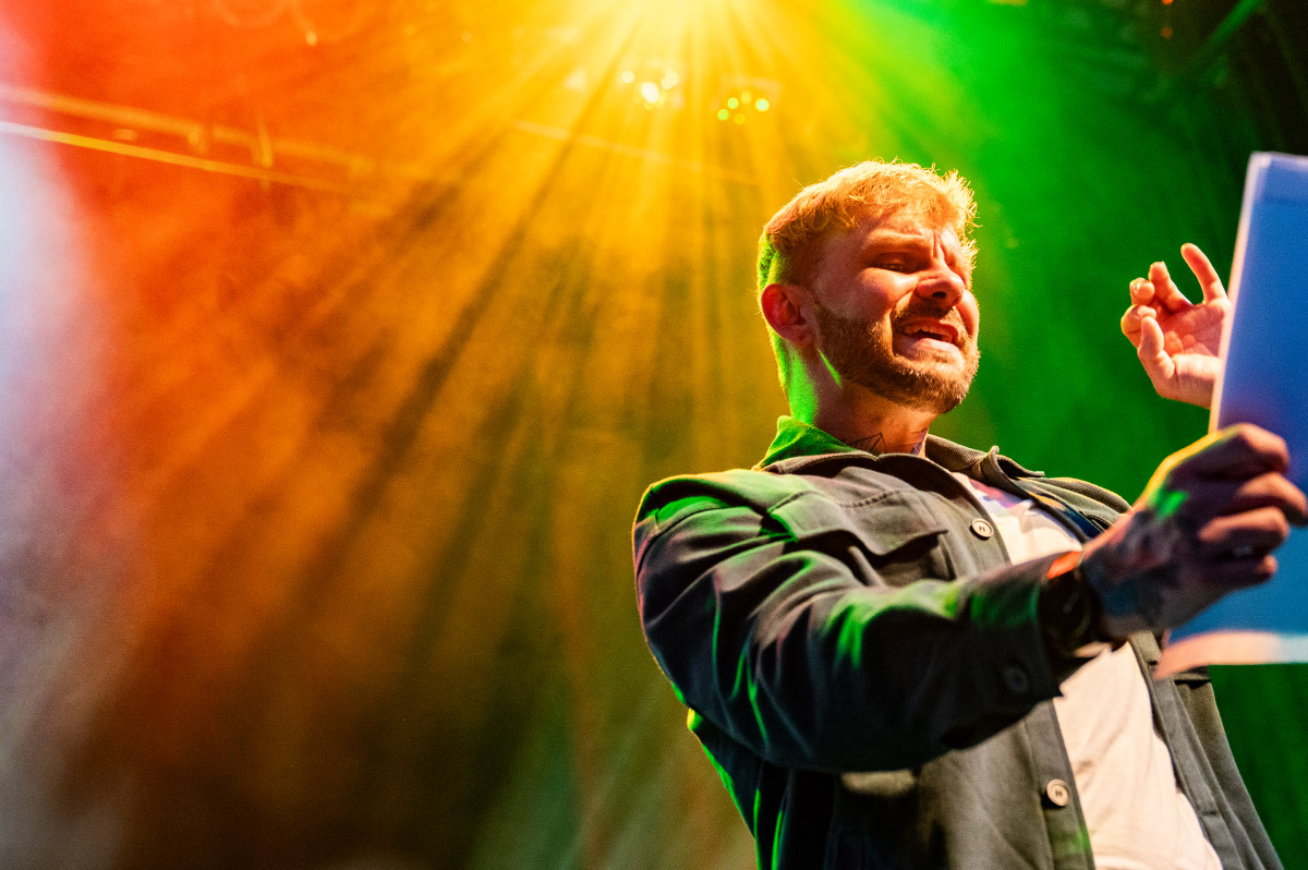 Poetry-Slammer hält Zettel in der Hand und spricht in Mikrofon - WestLotto
