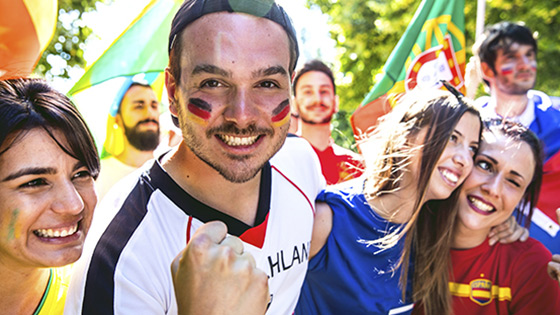 Gruppe von Fußballfans in verschiedenen Trikots mit Fahnen und Gesichtsbemalung im Freien.