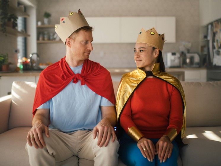 Ein Mann und eine Frau sitzen mit einer Pappkrone auf einer Couch | WestLotto-Rubbellos Krone